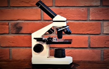 Microscopio de color blanco y negro sobre una base oscura en un fondo de ladrillo