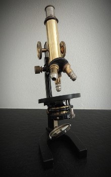 Microscopio antiguo de color negro y dorado sobre una mesa de color negro en un fondo blanco