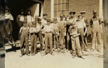 Grupo de obreros antiguos entre ellos niños parados afuera de una fabrica