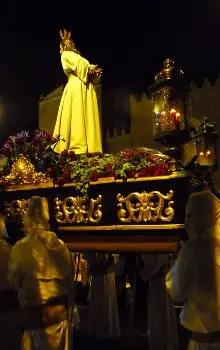Grupo de personas en procesión con la figura de Jesucristo en base de madera con flores