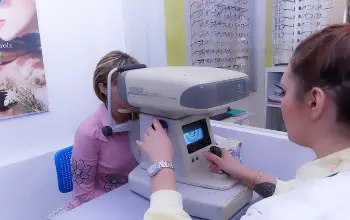 Optometrista realizando prueba examen en los ojos a una mujer con una maquina sobre una mesa gris en una óptica