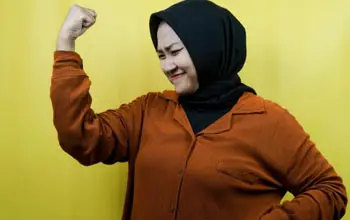 Mujer asiática feliz  con brazo levantado y puño cerrado en fondo amarillo