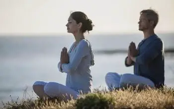 Hombre y mujer sentados al aire libre con las manos juntas en el pecho ojos cerrados meditando