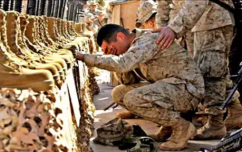 militar en cunclillas llorando en un memorial por los compañeros caidos