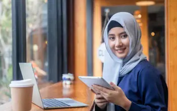 Una mujer musulmana en una cafetería trabajando con una laptop y una Tablet