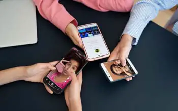 Manos de tres personas con teléfonos en las manos sobre una mesa de color negro