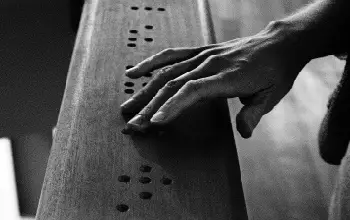Mano de una persona tocando el sistema Braille en madera en foto blanco y negro