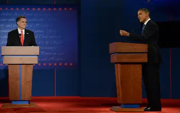 Debate entre dos hombres con trajes frente a podios de madera y micrófonos parados sobre una alfombra roja en un fondo de color azul