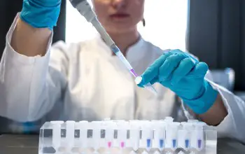 una mujer en bata de laboratorio y con guantes haciendo trabajando en un laboratorio