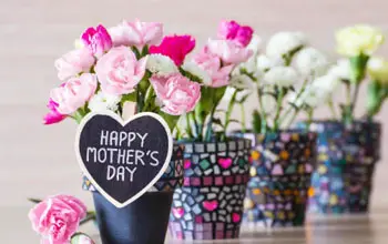 Macetas pequeñas decoradas con flores rosadas, blancas y fuccias con tarjeta de de feliz día de las madres en fondo borroso