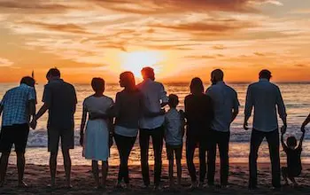 una gran familia de espaldas abrazados y agarrados de manos mientras ven la playa en el atardecer mostrando el sentido de pertenencia