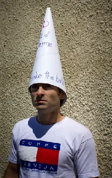 Hombre parado en un fondo de pared de cemento con un sombrero de cono sobre su cabeza