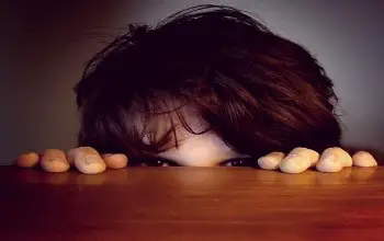 Niño con el rostro oculto tras una mesa de madera en un fondo de color gris
