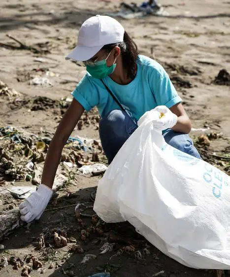 mujer con una bolsa y guantes agachada recogiendo basura del suelo