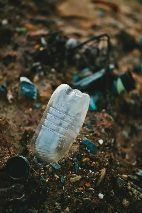 foto de cerca de una botella tirada y basura en la tierra