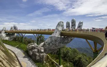 Escultura de dos manos enormes sosteniendo un puente colgante al aire libre en día soleado