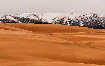 Vista aérea de persona caminando entre dunas y al fondo montañas con nieve