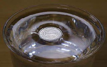 Moneda plateada flotando dentro de un recipiente transparente lleno de agua sobre una mesa de madera