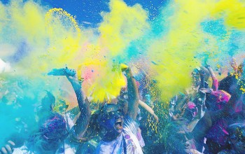 Grupo de personas celebrando en un festival, lanzando polvos de diferentes colores como amarillo, rosa y verde