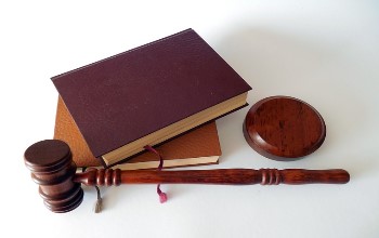 Libros de color marrón y martillo de la justicia con base de madera sobre un fondo blanco