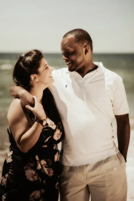 Hombre y mujer abrazados sonriendo caminando por la playa