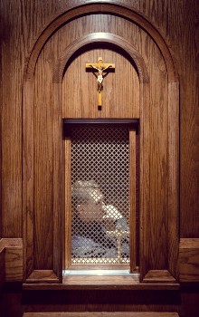 Sacerdote sentado dentro de un confesionario de madera